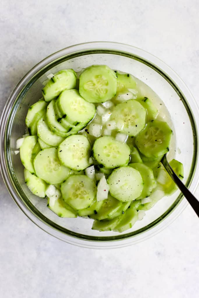 Vinegar cucumber salad in clear glass bowl with fresh cracked pepper on top and spoon