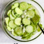 Vinegar cucumber salad in clear glass bowl with fresh cracked pepper on top and spoon