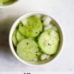 Vinegar cucumber salad in small white bowl with fresh cracked pepper on top