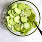 Vinegar cucumber salad in clear glass bowl with fresh cracked pepper on top and spoon