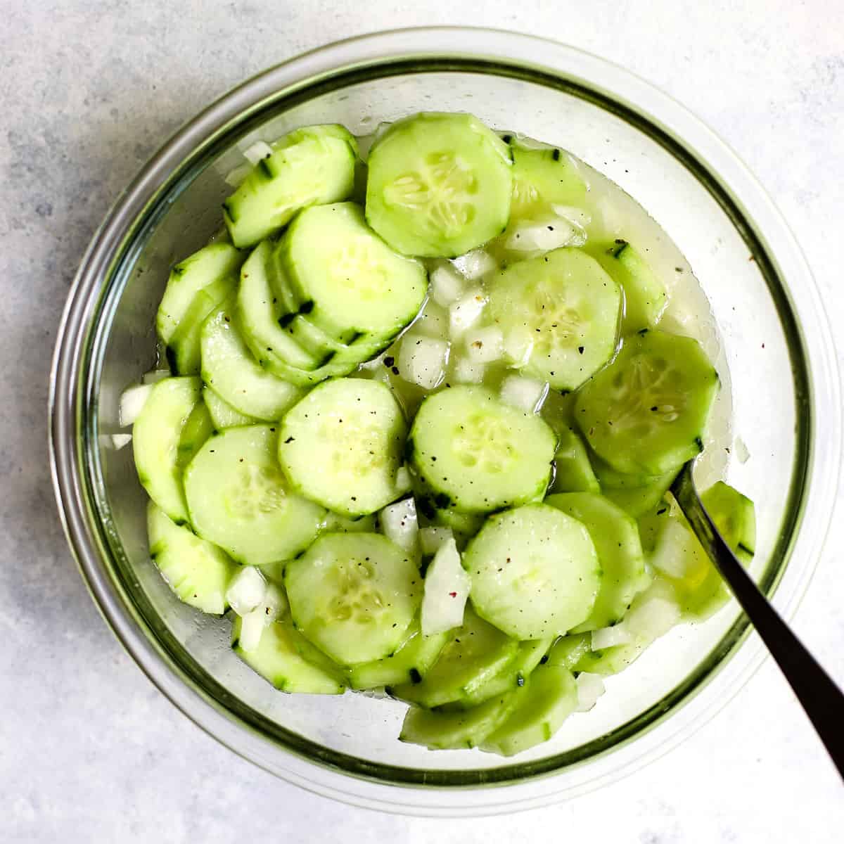 Vinegar cucumber salad in clear glass bowl with fresh cracked pepper on top and spoon