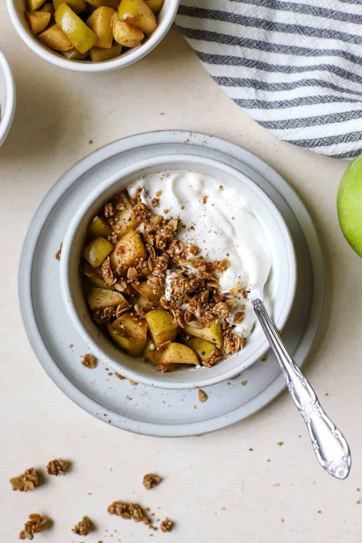 Apple pie yogurt bowl with spoon, resting on small blue plate.