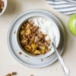 Apple pie yogurt bowl with spoon, resting on small blue plate.