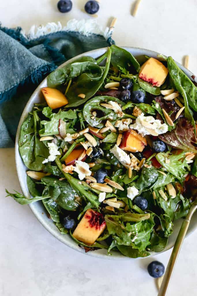 Peach blueberry and goat cheese salad tossed together in a serving bowl.