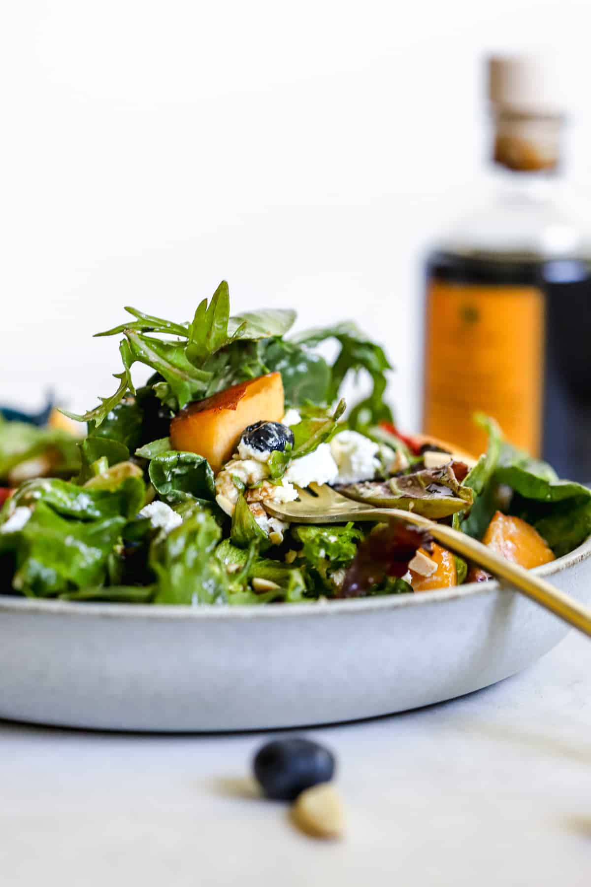 Peach blueberry salad with fork spearing a peach, in light blue bowl with aged balsamic in background