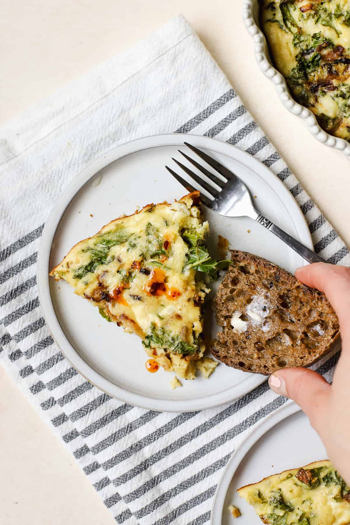 Slice of crustless kale pie on small plate with buttered sourdough and fork.