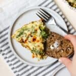 Slice of crustless kale pie on small plate with buttered sourdough and fork.