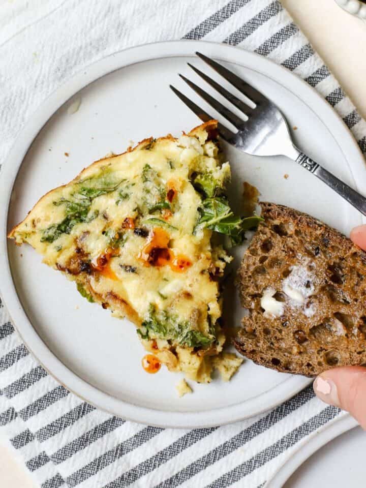 Slice of crustless kale pie on small plate with buttered sourdough and fork.