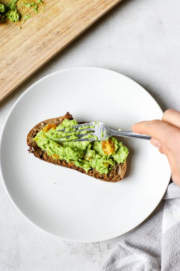 Hand transferring avocado mash to sourdough toast.