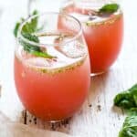 Two glasses of watermelon agua fresca garnished with fresh mint leaf.