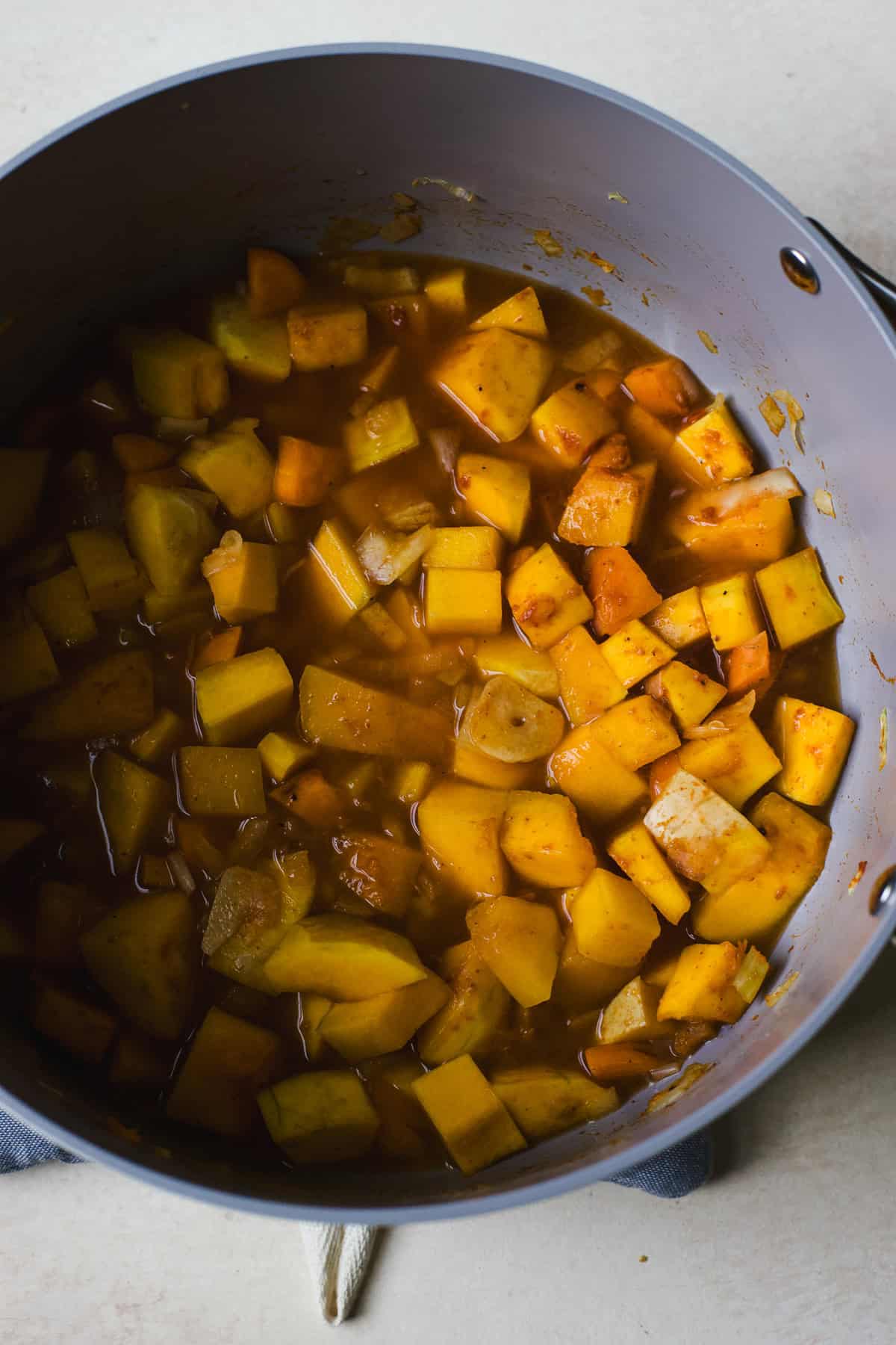 Adding vegetable broth to a large soup pot with butternut squash soup ingredients.