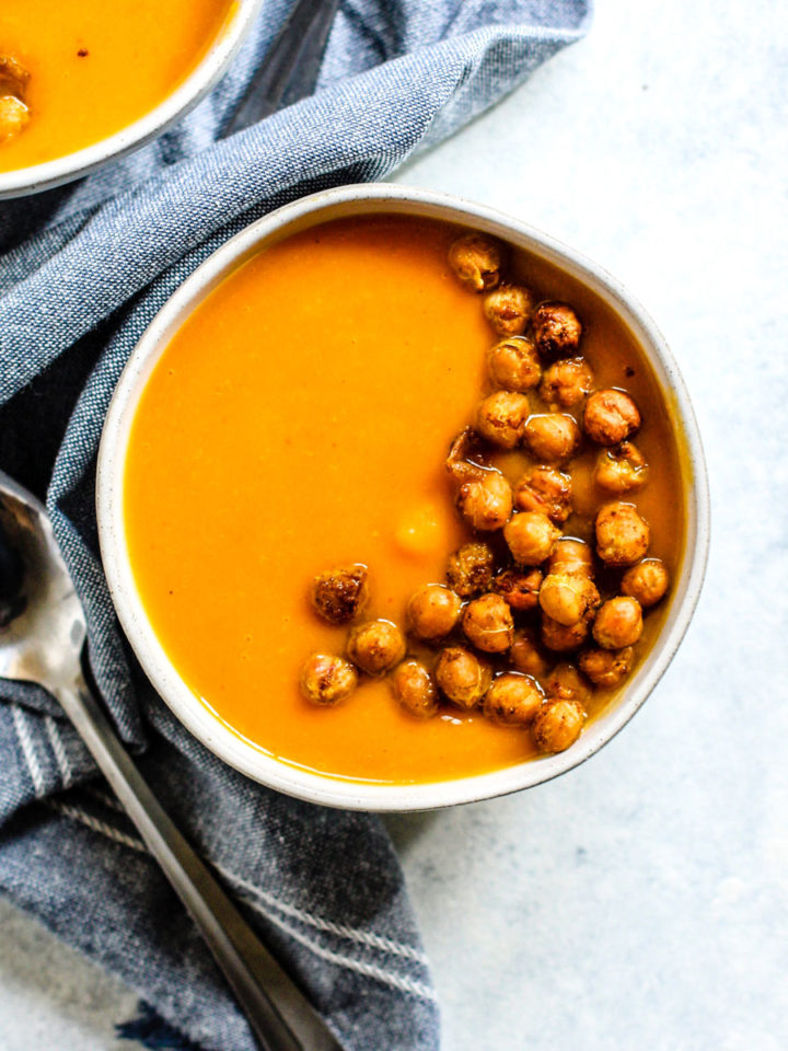 Thai-spiced butternut bisque in white ceramic bowl with curry roasted chickpeas, with denim blue linen on the side