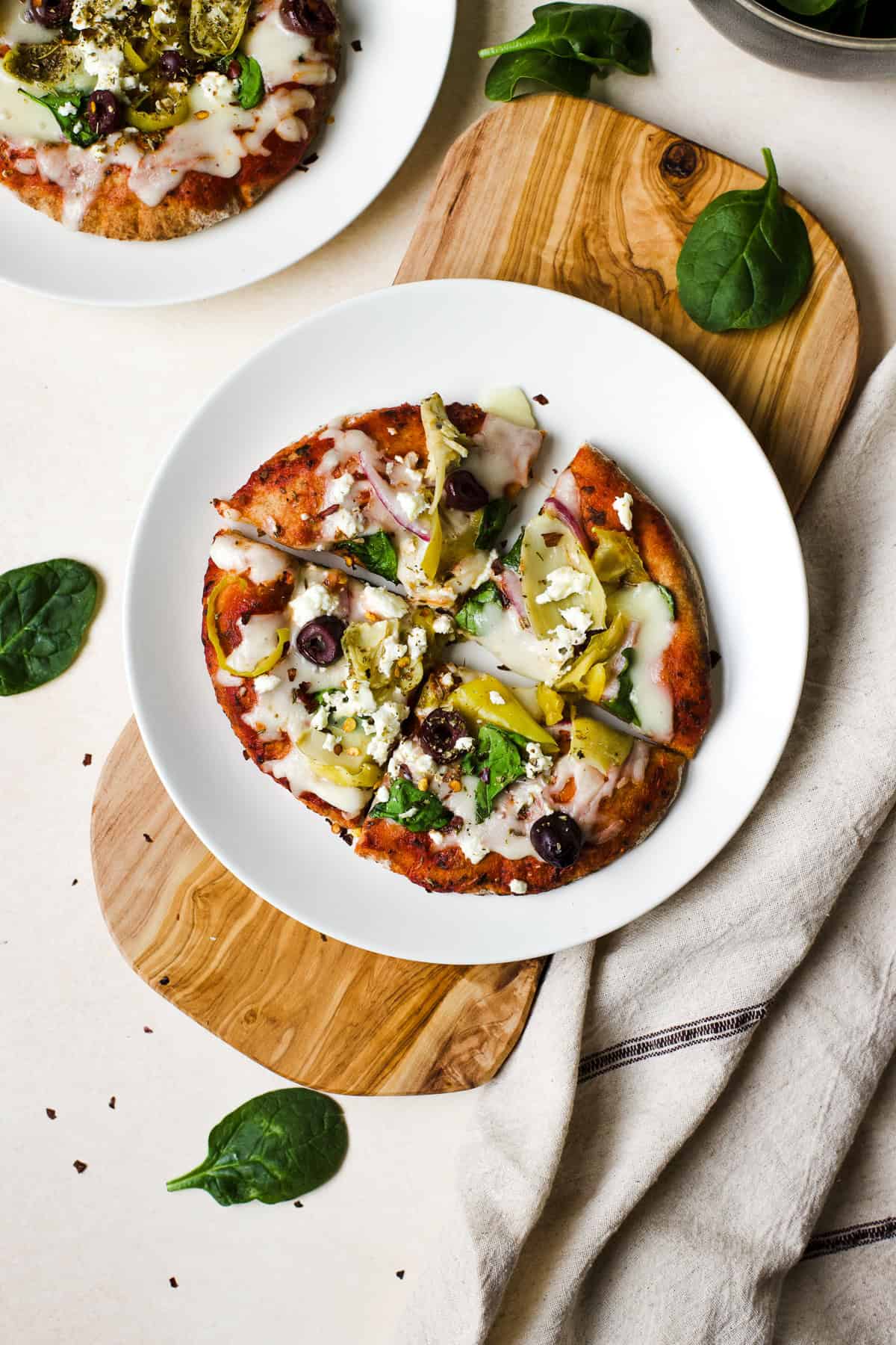 Greek pita pizza fresh out of the oven, sliced into four pieces on a white plate.