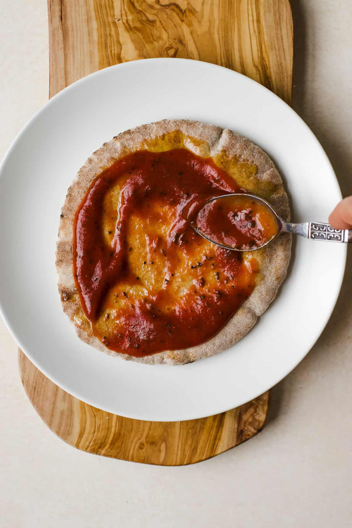Pita bread with pizza sauce being spread on top.