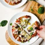 Greek pita pizza slices on white plate with hand picking up a slice.