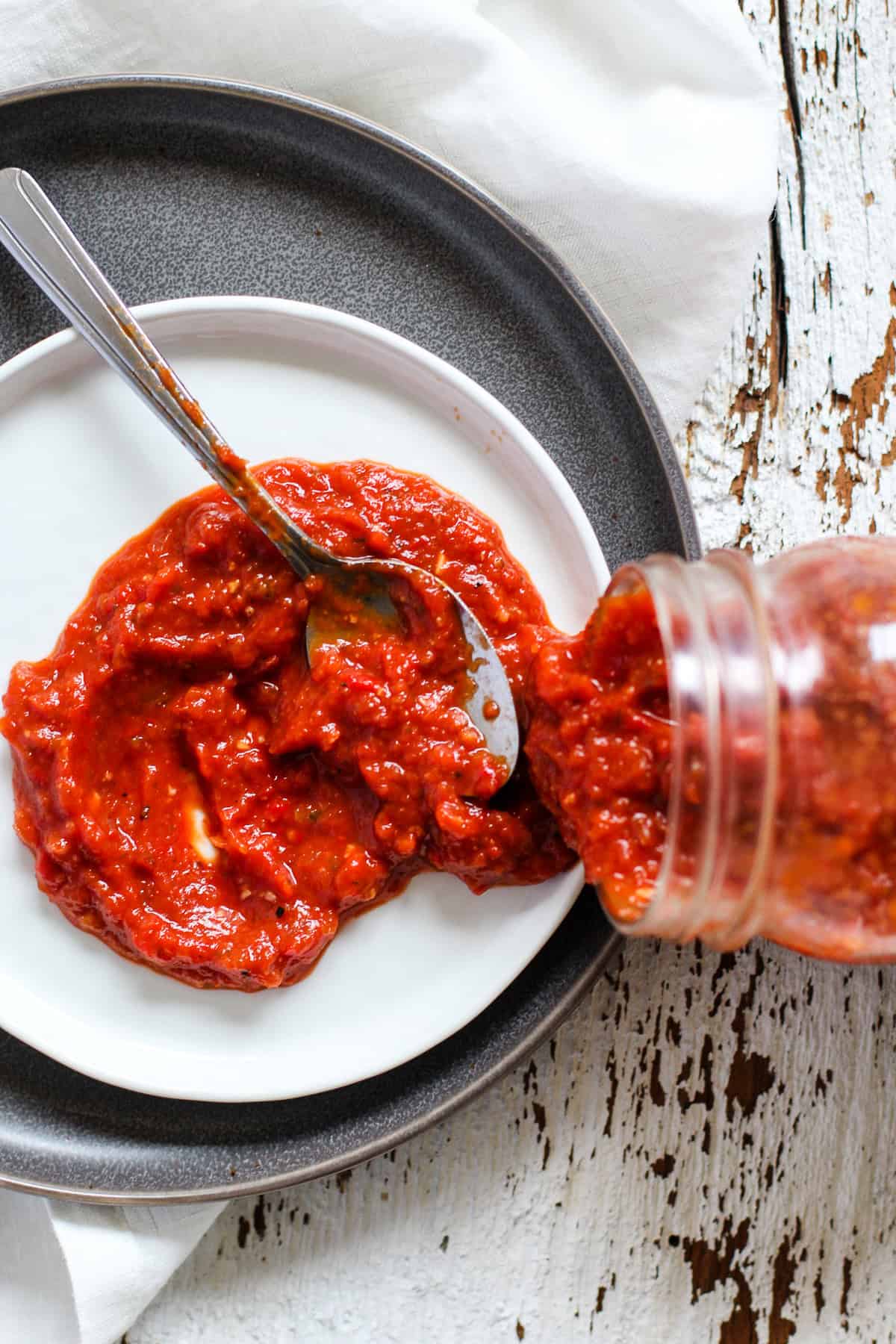 Roasted red pepper pizza sauce poured out from glass jar onto white plate with spoon.