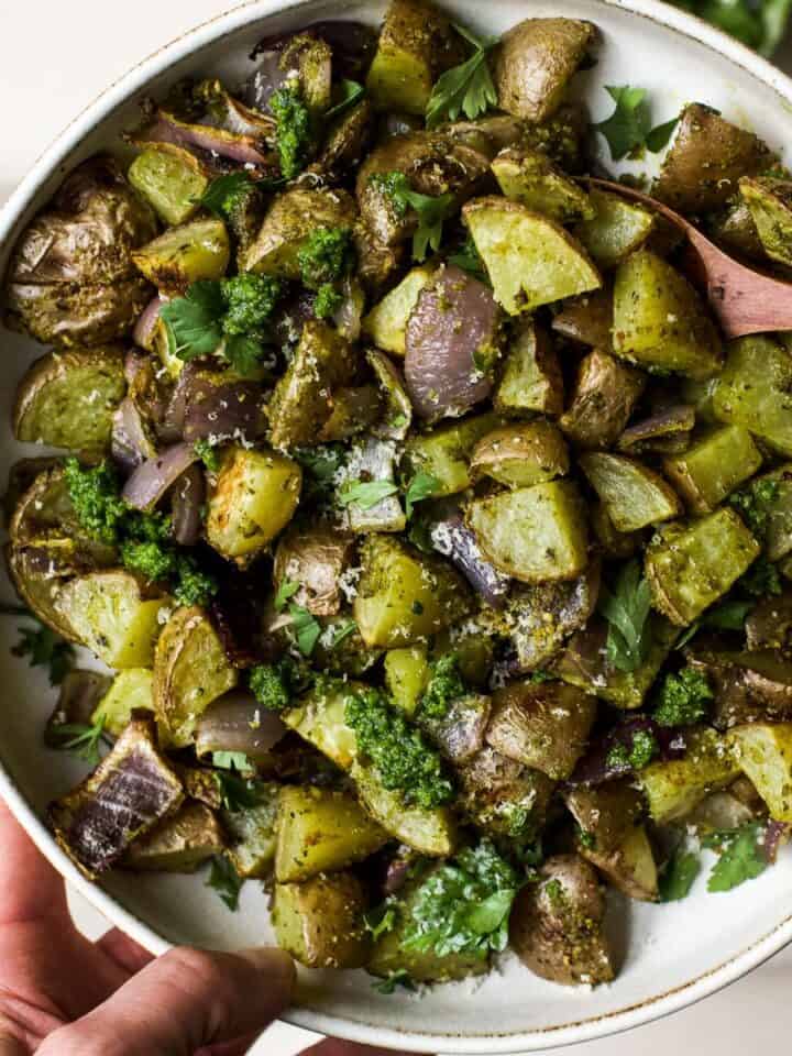 Pesto roasted potatoes in white bowl with spoon.