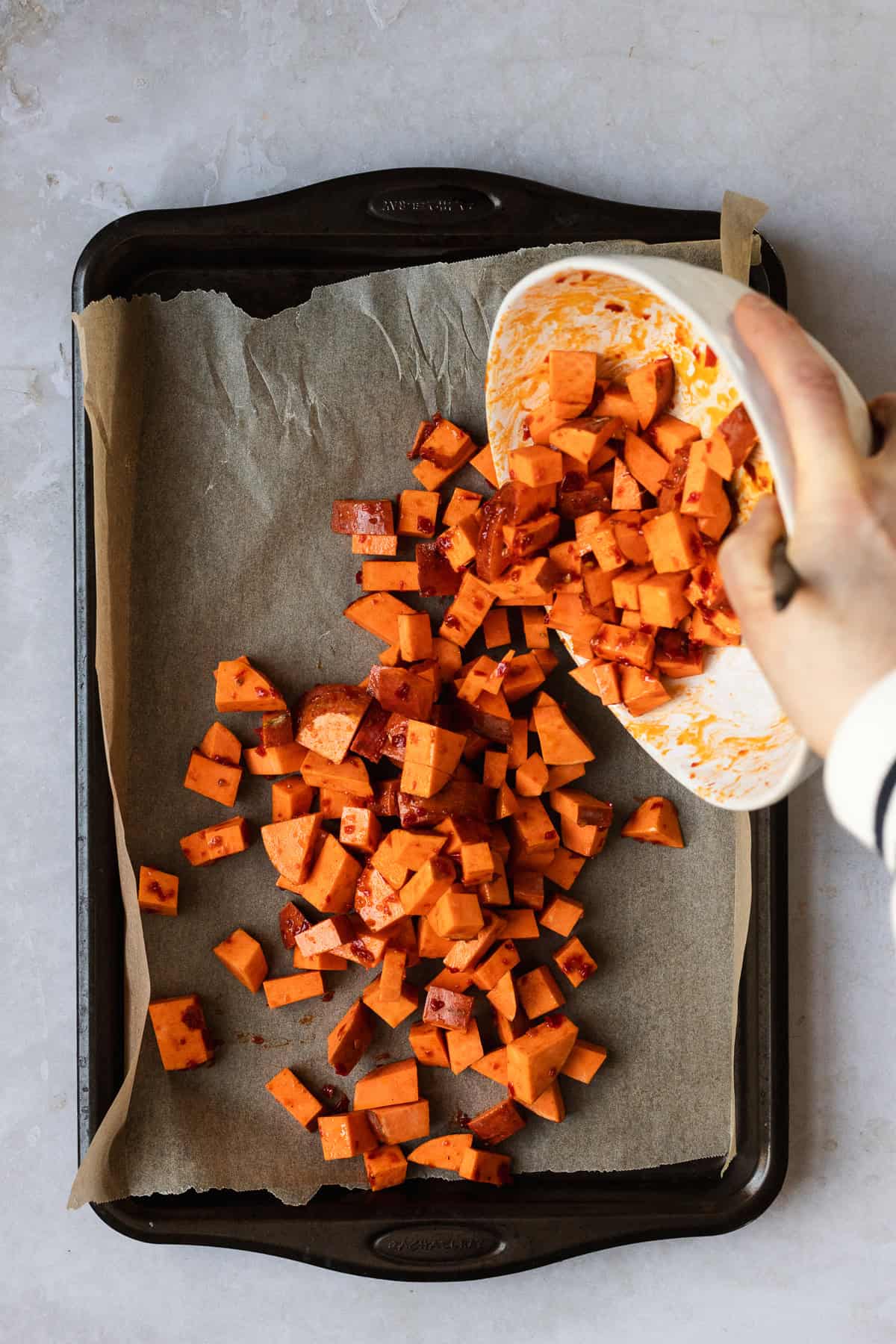 Sweet potato cubes seasoned with harissa paste being dumped onto sheet pan.