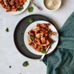 Harissa roasted sweet potatoes drizzled with tahini sauce on a plate.