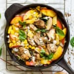 Peach basil balsamic chicken in a cast iron skillet with fresh basil and goat cheese, on top of a white linen napkin on a white farmhouse-style surface