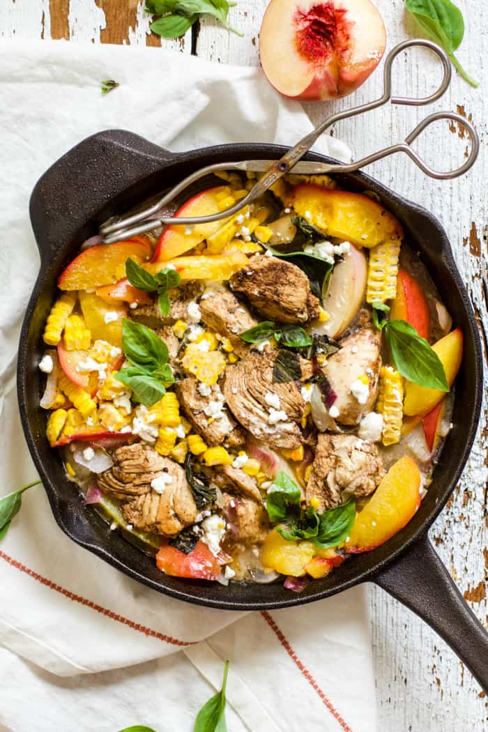 Peach basil balsamic chicken in a cast iron skillet with fresh basil and goat cheese, on top of a white linen napkin on a white farmhouse-style surface