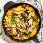 Peach basil balsamic chicken in a cast iron skillet with fresh basil and goat cheese, on top of a white linen napkin on a white farmhouse-style surface