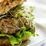 Close-up of turkey pesto walnut burger on sprouted grains roll with sprouts, lettuce, and avocado