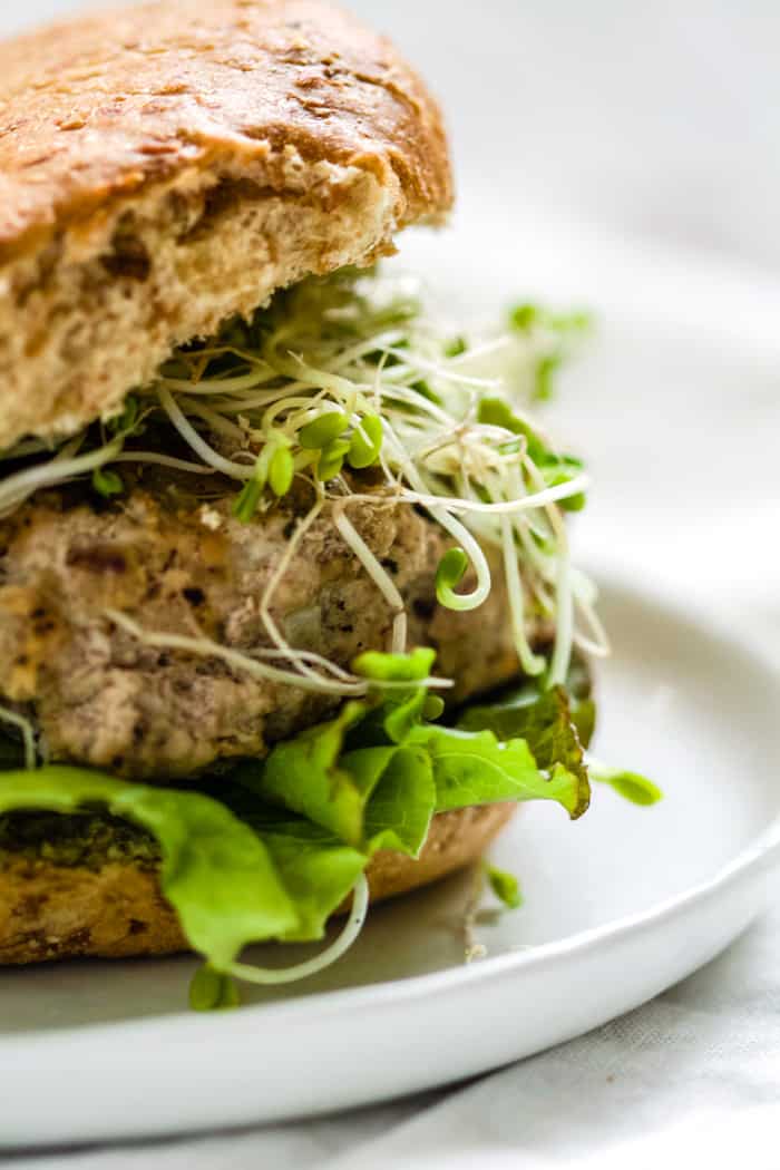 Close-up of turkey pesto walnut burger on sprouted grains roll with sprouts, lettuce, and avocado