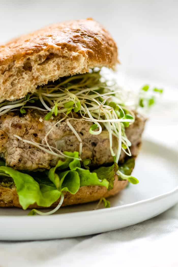 Close-up of turkey pesto walnut burger on sprouted grains roll with sprouts, lettuce, and avocado