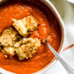 Bowl of harissa tomato soup with pepper jack grilled cheese croutons