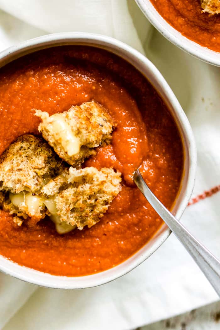 Bowl of harissa tomato soup with pepper jack grilled cheese croutons