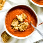 Bowl of harissa tomato soup with pepper jack grilled cheese croutons