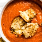 Bowl of harissa tomato soup with pepper jack grilled cheese croutons