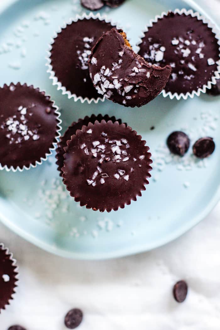 Salted dark chocolate pumpkin peanut butter cups on light blue plate and white linen, with scattered chocolate chips