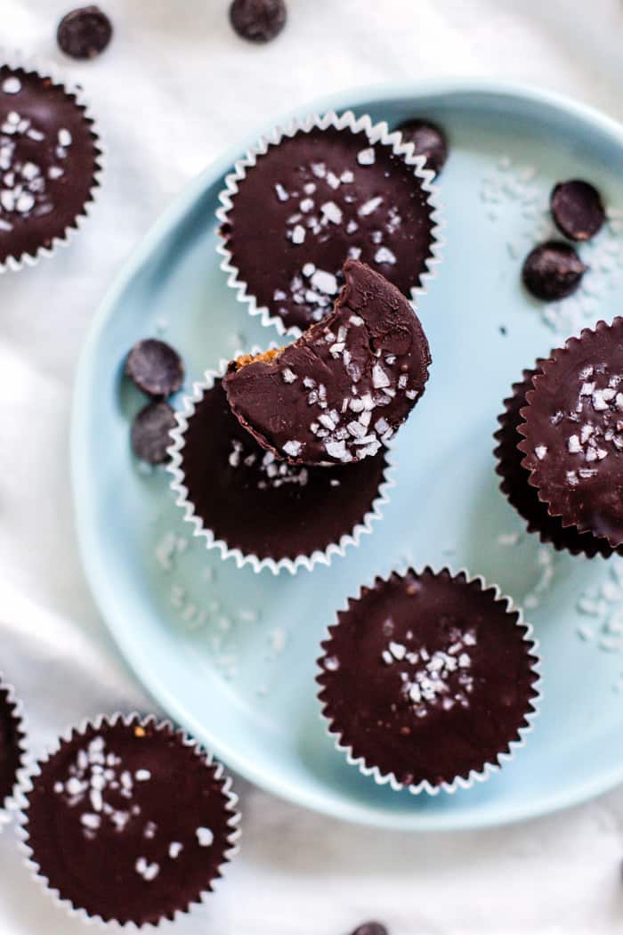 Salted dark chocolate pumpkin peanut butter cups on light blue plate and white linen, with scattered chocolate chips