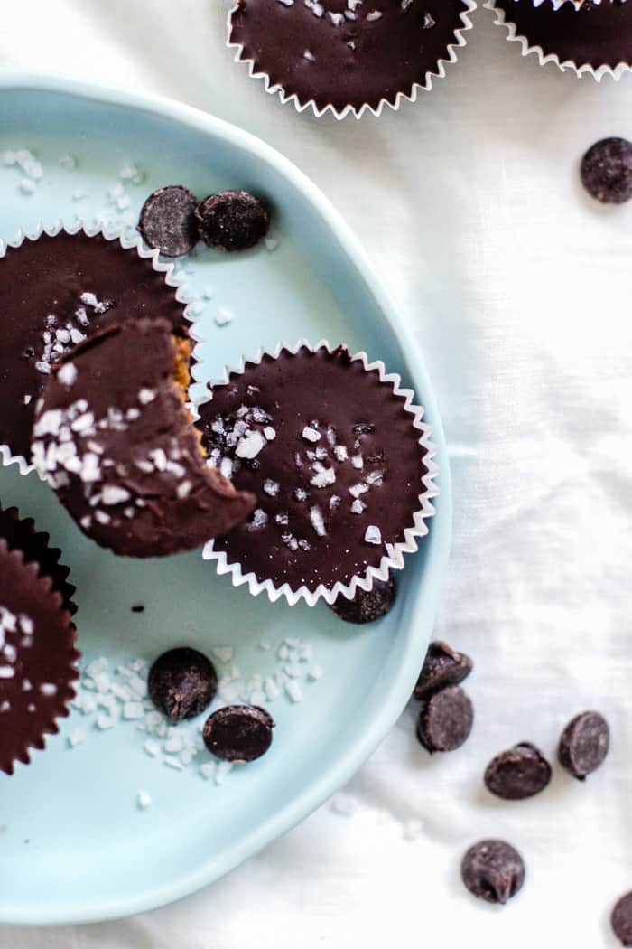 Salted dark chocolate pumpkin peanut butter cups on light blue plate and white linen, with scattered chocolate chips