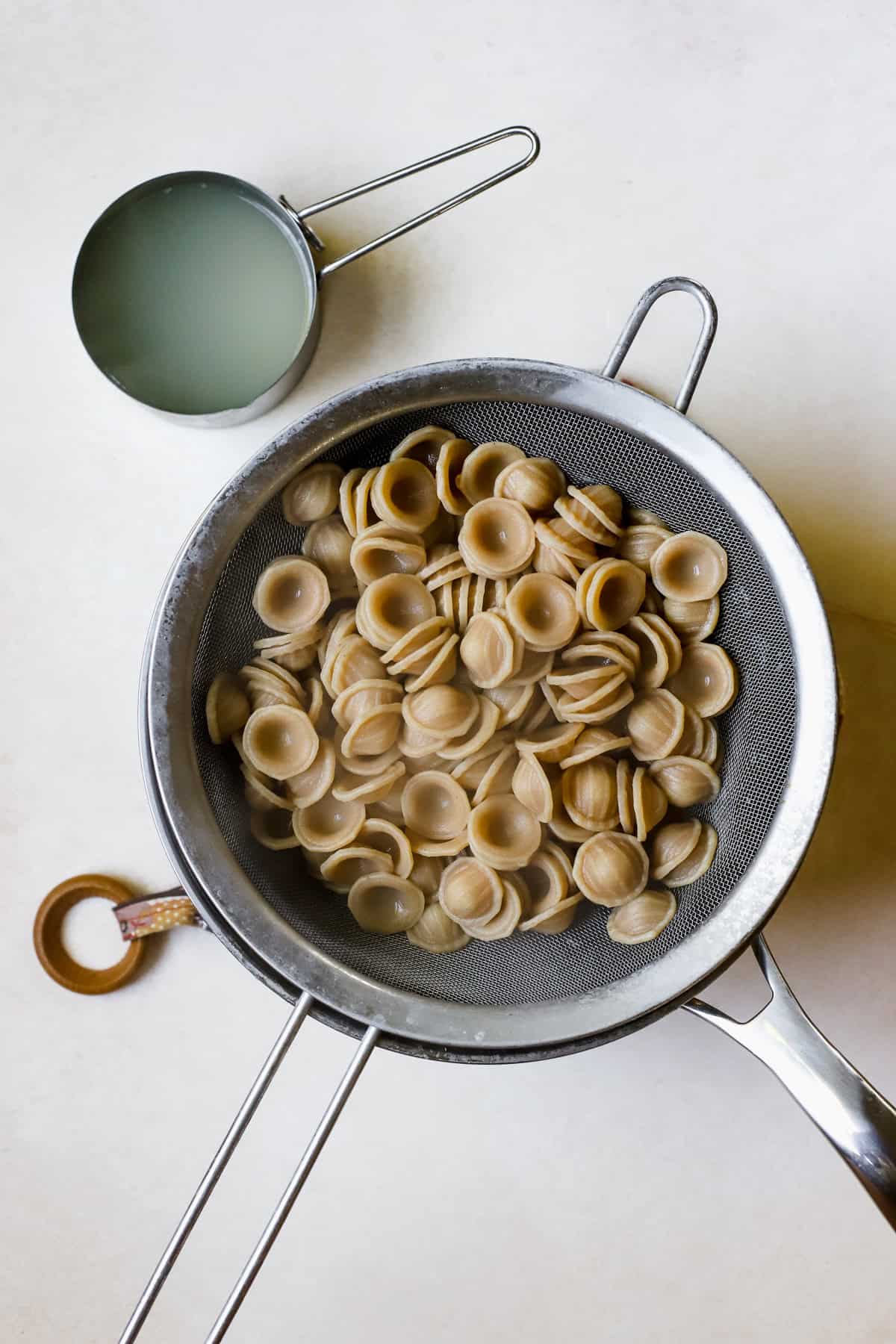 Cooked orecchiette being drained with reserved pasta water set aside.