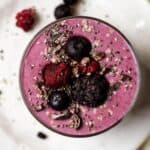 High protein berry smoothie in a glass, topped with berries, chia seeds, and cacao nibs.