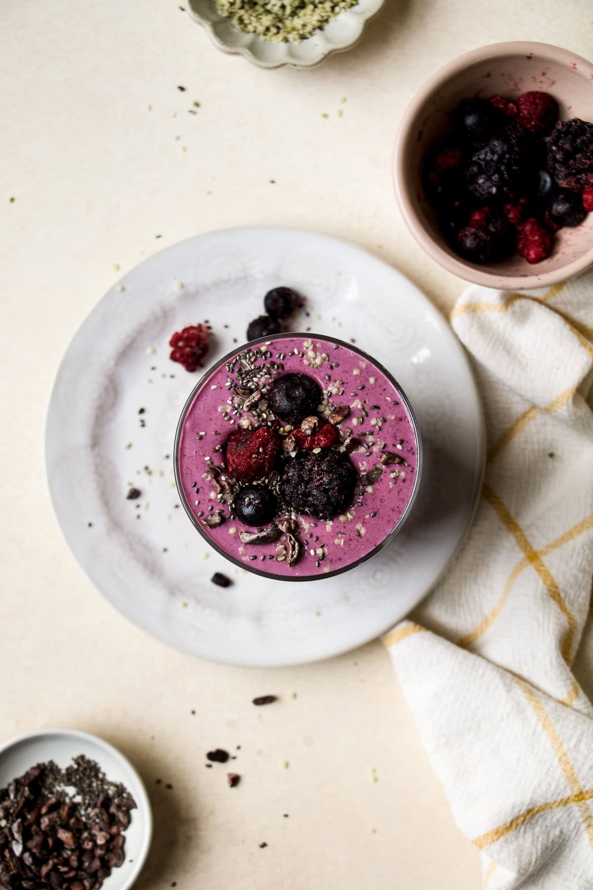 High protein berry smoothie in a glass, topped with berries, chia seeds, and cacao nibs.