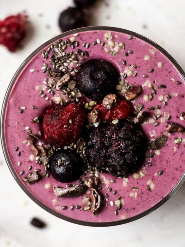 High protein berry smoothie in a glass, topped with berries, chia seeds, and cacao nibs.