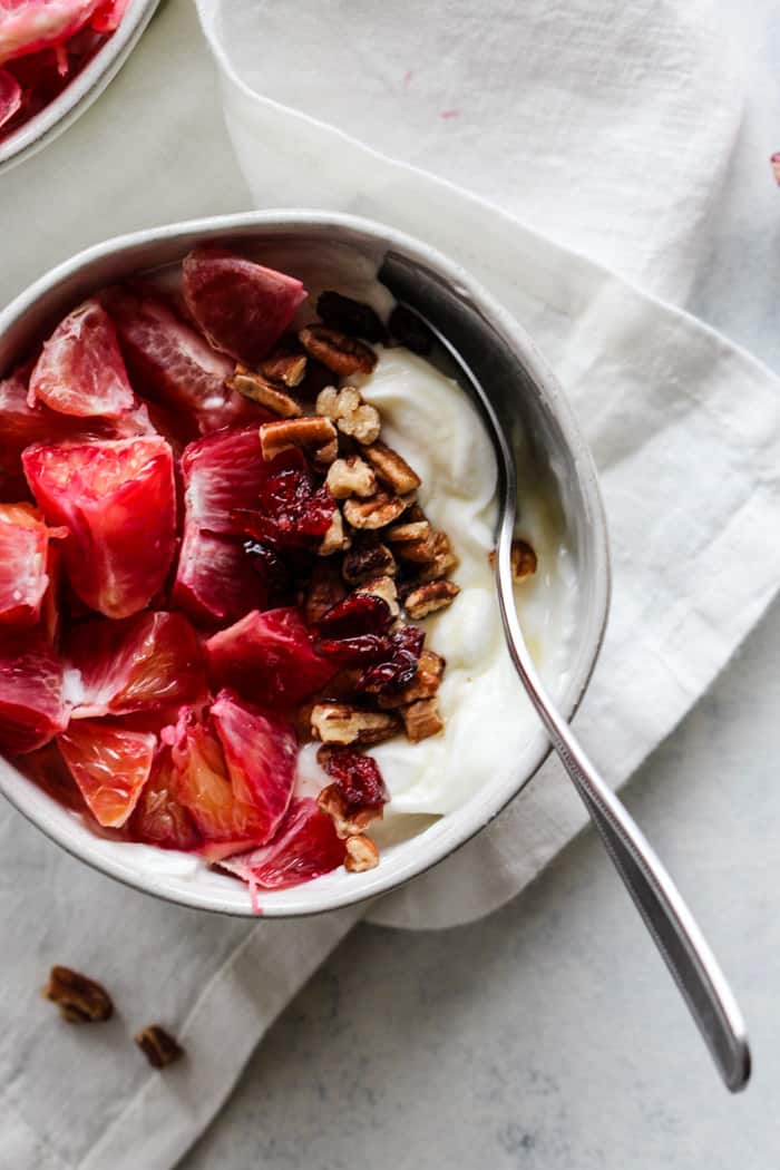 Blood orange maple pecan yogurt bowl in white bowl on white napkin