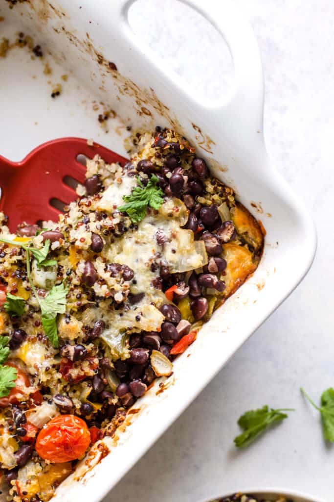 Cheesy black bean quinoa casserole in white baking dish with red spatula