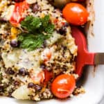 Cheesy black bean quinoa casserole in white baking dish with red spatula