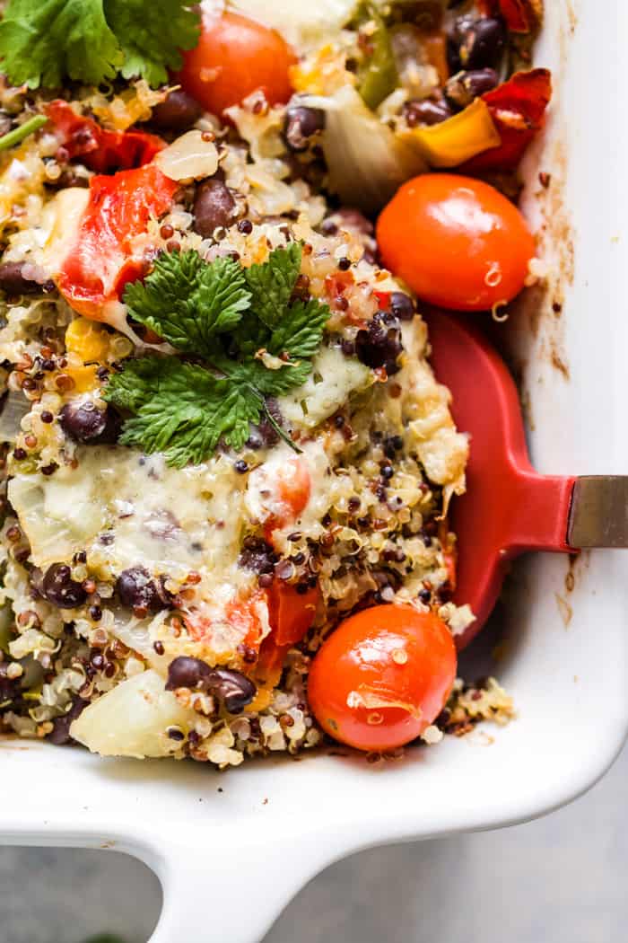 Cheesy black bean quinoa casserole in white baking dish with red spatula