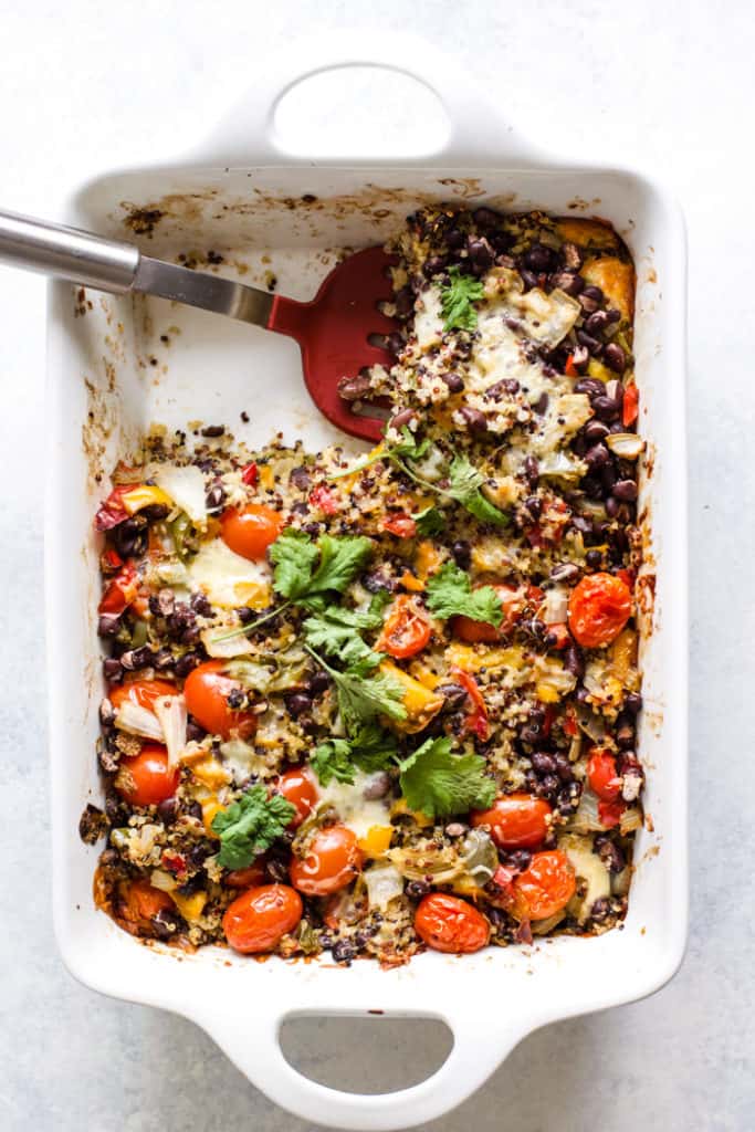 Cheesy black bean quinoa casserole in white baking dish with red spatula