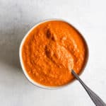 Romesco sauce in small white ball with spoon, on light blue and white surface