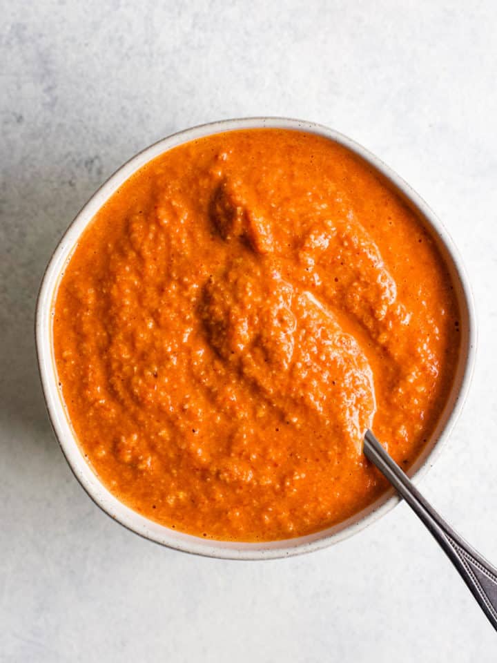 Romesco sauce in small white ball with spoon, on light blue and white surface