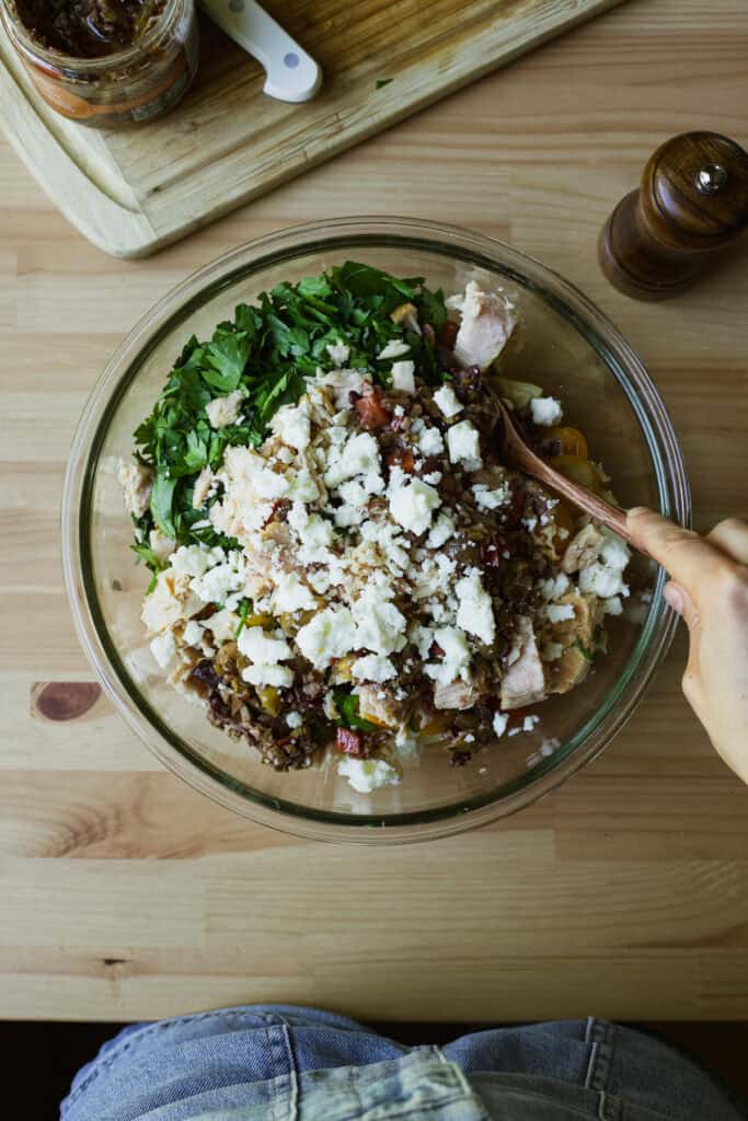 Mixing olive and tuna pasta salad together in a bowl.