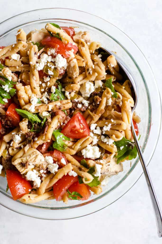 Olive tapenade and tuna pasta salad in clear bowl with spoon