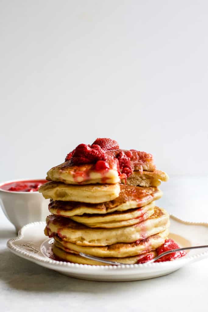 Stack of whole wheat Greek yogurt pancakes with strawberry compote on top, on white plate with fork.